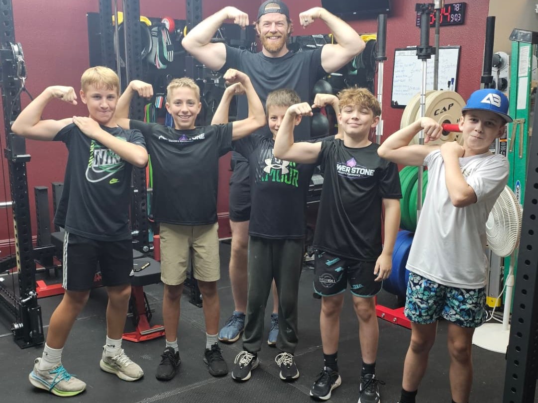 Coach Conor Adams and a group of youth athletes flexing their muscles after a training session