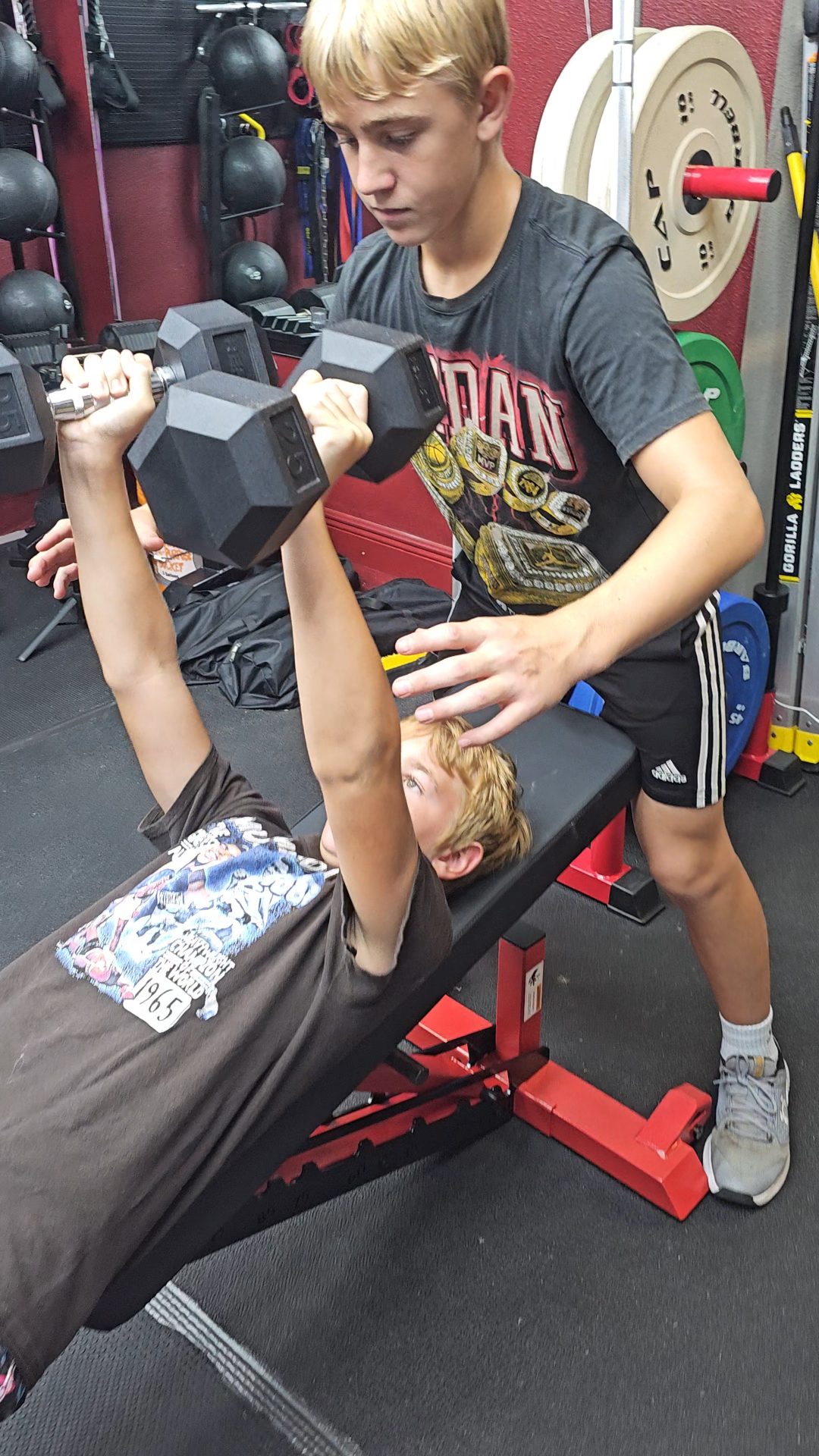 Teen athlete spotting another student on the dumbbell bench press
