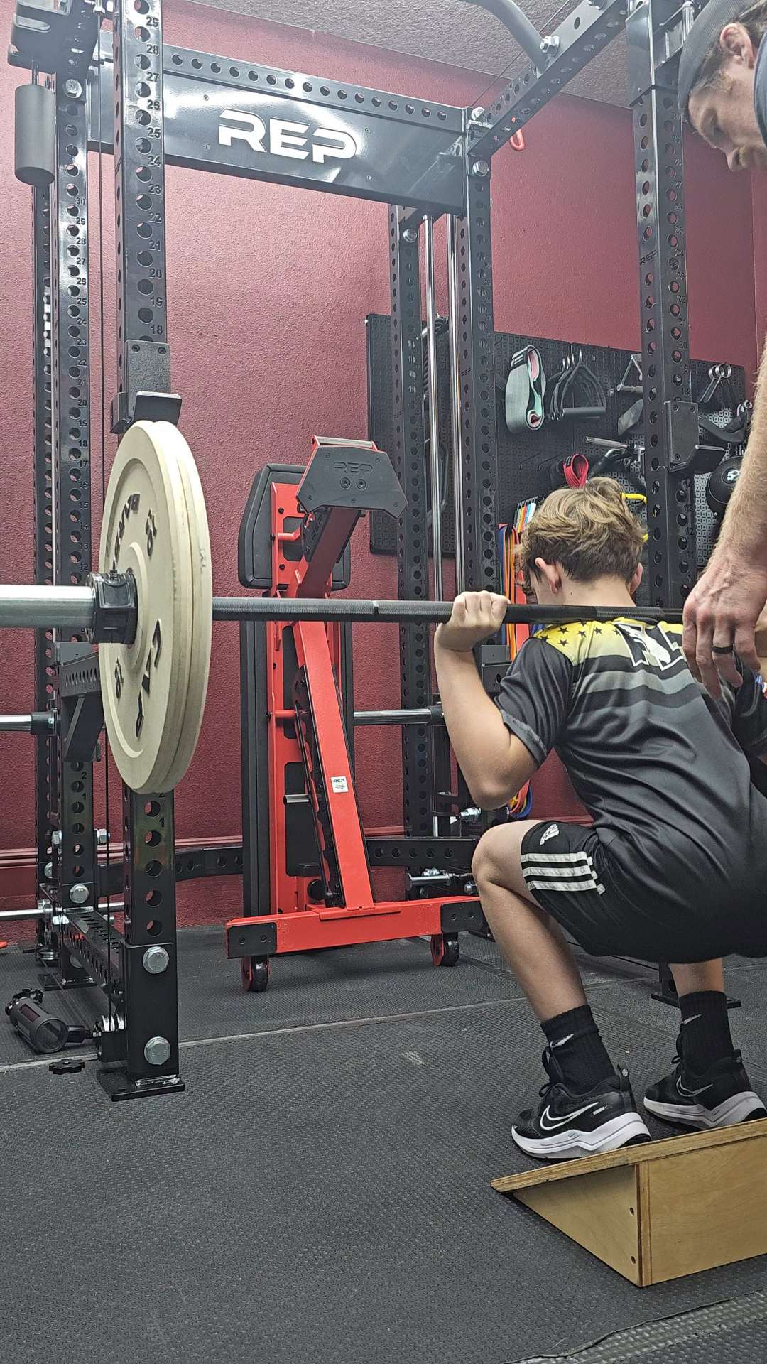 Youth athlete back squatting with coach spotting at Power Stone